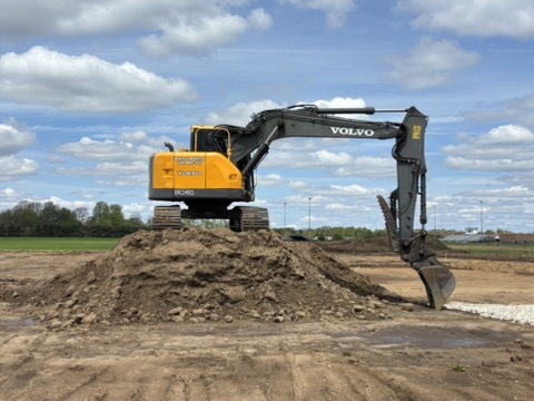 Excavator at work with open field and trees in the distance